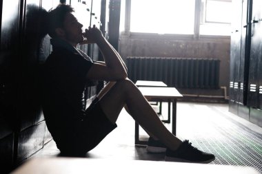 Genç atletik beyaz adam, spor yaptıktan sonra soyunma odasında yalnız başına dinleniyor..