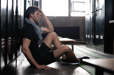 Genç atletik beyaz adam, spor yaptıktan sonra soyunma odasında yalnız başına dinleniyor..