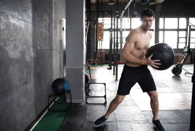 Genç, formda, kaslı ve formda bir adam spor salonunda sıkı antrenman yapmak için duvarlara ilaç fırlatıyor.