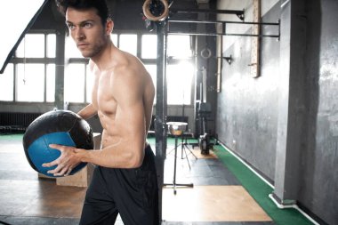 Genç, formda, kaslı ve formda bir adam spor salonunda sıkı antrenman yapmak için duvarlara ilaç fırlatıyor.