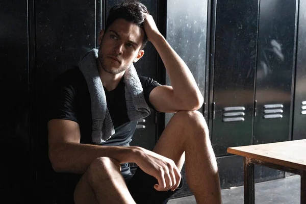 Joven atlético hombre caucásico sentado solo en el vestuario oscuro gimnasio descansando después del entrenamiento. —  Fotos de Stock