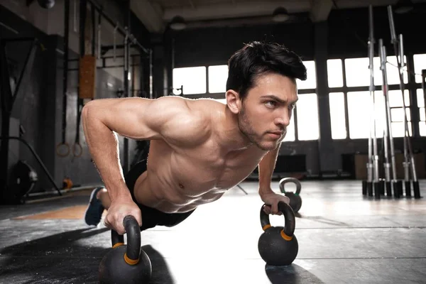 Yakışıklı, kaslı bir adam halter egzersizinde halterle şınav çekiyor..