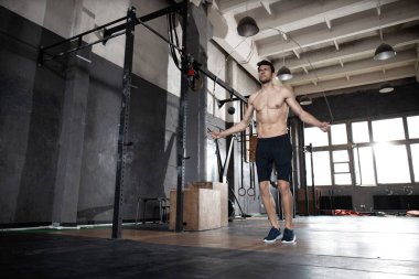 Genç sporcu spor salonunda ip atlama egzersizi yapıyor..