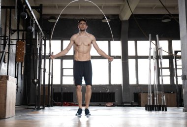 Genç sporcu spor salonunda ip atlama egzersizi yapıyor..