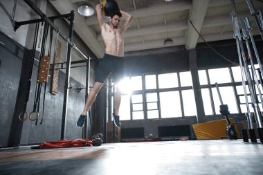 Formda bir adam top fırlatıyor, spor salonu zeminine ya da omuzlarına vuruyor, vücut egzersizi yapıyor.