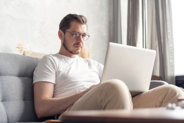Yeni blog yazıları yazılıyor. Yakışıklı genç adam evdeki kanepede otururken bilgisayarını gülümseyerek kullanıyor..