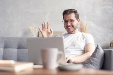 Evdeki kanepede otururken dizüstü bilgisayarda sohbet eden mutlu genç adam..