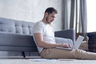 Dizüstü bilgisayarda çalışan bir adam günlüğü ve resmi evraklarıyla yerde oturuyor.