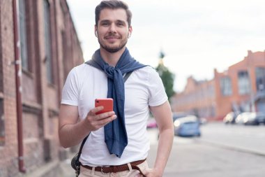 Yakışıklı gülümseyen adam şehirde yürürken müzik dinliyor.