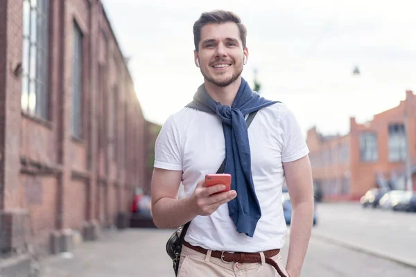 Bonito homem sorridente ouvindo música enquanto caminhava na cidade — Fotografia de Stock