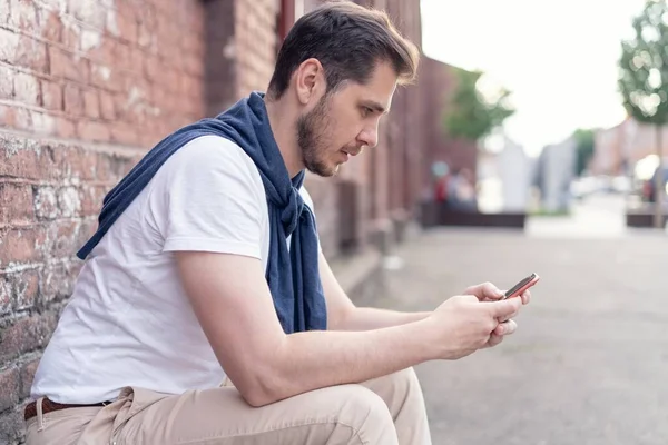 Homem moderno hipster bonito usando smartphone na cidade . — Fotografia de Stock