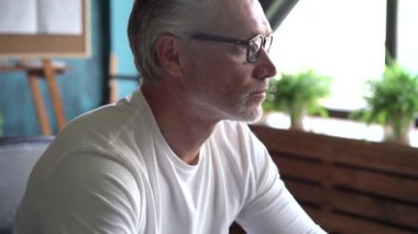 Ofiste çalışan bilgisayar kullanan kıdemli serbest çalışan. Gülümseyen gri saçlı gözlüklü adam bilgisayarda yazı yazıyor.