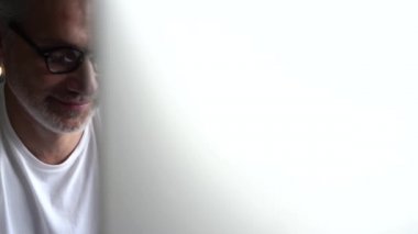 Ofiste çalışan bilgisayar kullanan kıdemli serbest çalışan. Gülümseyen gri saçlı gözlüklü adam bilgisayarda yazı yazıyor.