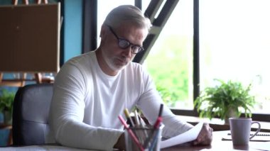 Ofiste çizimlerle çalışan olgun beyaz bir mimar. Profesyonel adam yeni bina geliştirme projesi üzerinde çalışıyor