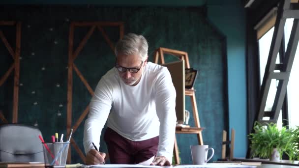 Зрелый кавказский архитектор, работающий с чертежами в офисе. Над проектом застройки нового дома трудится местный житель — стоковое видео