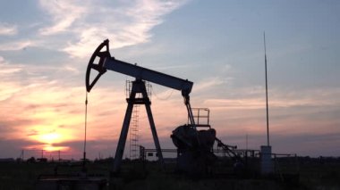 Gün batımında petrol sahasında çalışan yağ pompasının silueti. Endüstriyel ekipman.