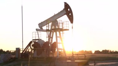 Gün batımında petrol sahasında çalışan yağ pompasının silueti. Endüstriyel ekipman.