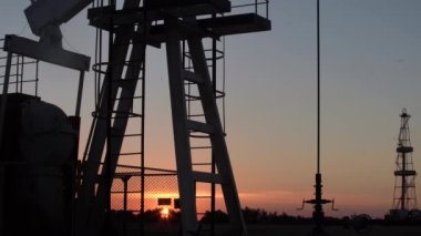 Gün batımında petrol sahasında çalışan yağ pompasının silueti. Endüstriyel ekipman.