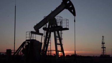 Gün batımında petrol sahasında çalışan yağ pompasının silueti. Endüstriyel ekipman.