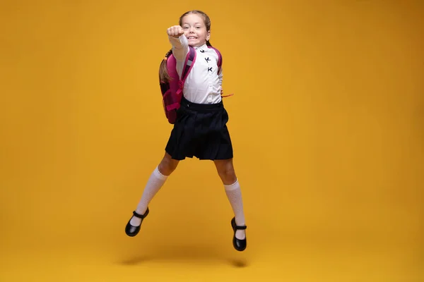 Menina da escola alegre saltando sobre fundo amarelo. Felicidade, atividade e conceito de criança. — Fotografia de Stock