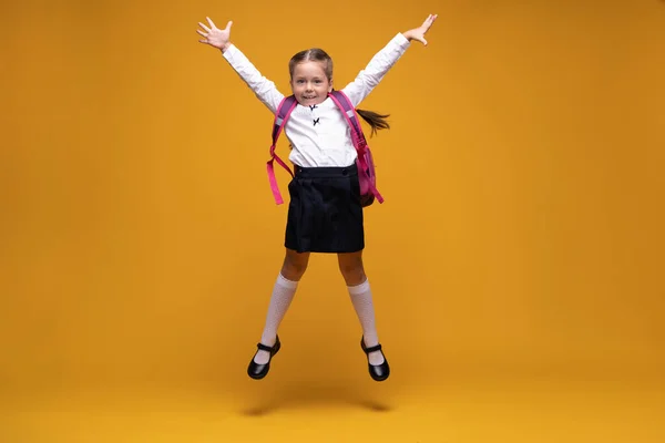 Fröhliche kleine Schulmädchen springen über gelben Hintergrund. Glück, Aktivität und Kinderkonzept. — Stockfoto