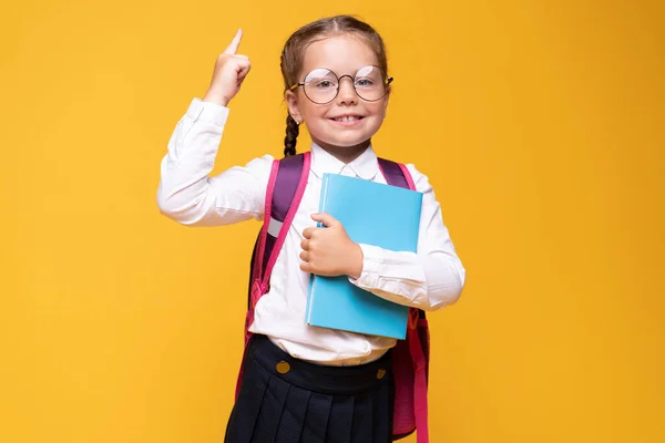 Kleines Mädchen mit Schulrucksack, erhobener Zeigefinger, Ideenkonzept. — Stockfoto