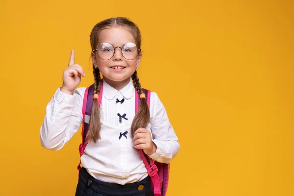 Niña con mochila escolar apuntando con el dedo hacia arriba, concepto de idea. —  Fotos de Stock