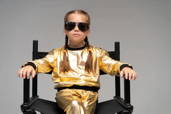 A little girl in gold suit sits on a chair. Isolated on a yellow background. — Stock Photo, Image