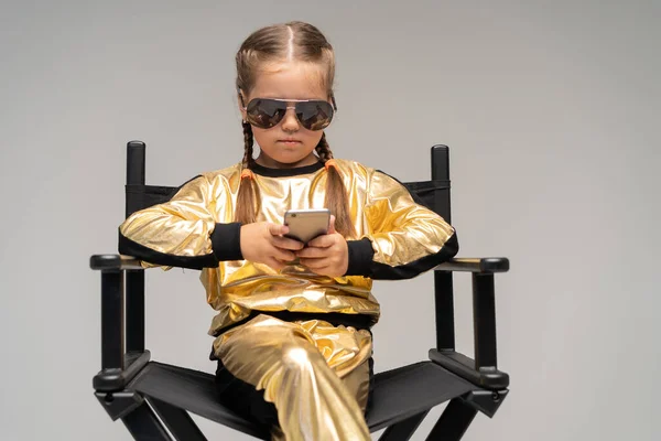 Altın takım elbiseli küçük bir kız sandalyede oturuyor. Sarı arka planda izole edilmiş.. — Stok fotoğraf