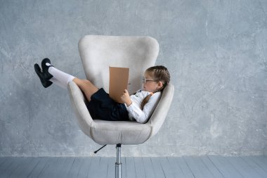 Kitap okumaya odaklanmış liseli bir kız koltuğa oturur..