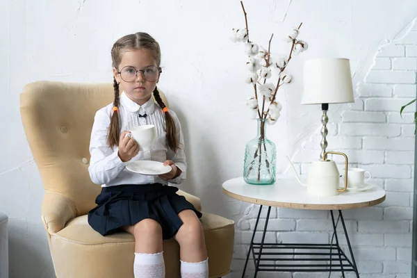 School girl in uniform sit in armchair and drinking a tea. — Stock Photo, Image