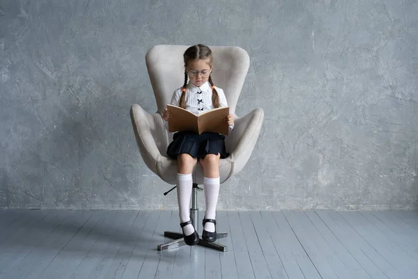 École fille axée sur la lecture livre assis dans le fauteuil. — Photo