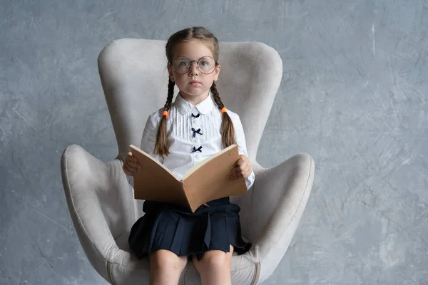 Szkoła dziewczyna koncentruje się na czytaniu książki siedzieć w fotelu. — Zdjęcie stockowe