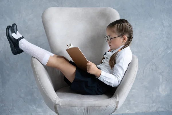 Schulmädchen konzentriert sich auf das Lesen Buch sitzen im Sessel. — Stockfoto