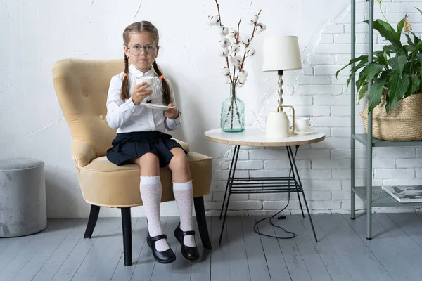 Escuela chica en uniforme sentarse en sillón y beber un té. —  Fotos de Stock