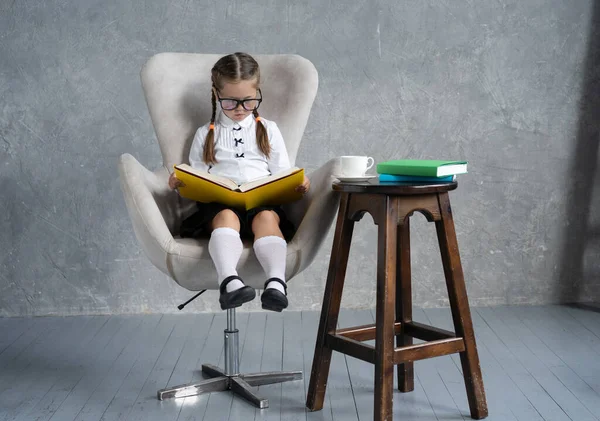 Escola menina focada na leitura livro sentar em poltrona. — Fotografia de Stock