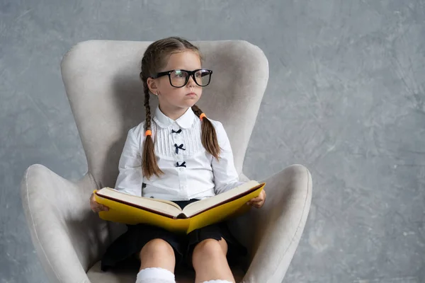 Escola menina focada na leitura livro sentar em poltrona. — Fotografia de Stock