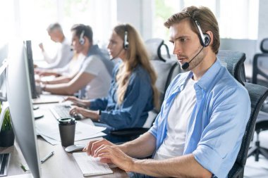 Çağrı merkezinde çalışan, kulaklık takan genç, yakışıklı bir erkek müşteri destek operatörü.