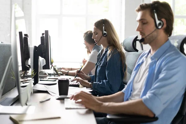 Jovem bonito masculino suporte ao cliente telefonista com fone de ouvido trabalhando no call center — Fotografia de Stock