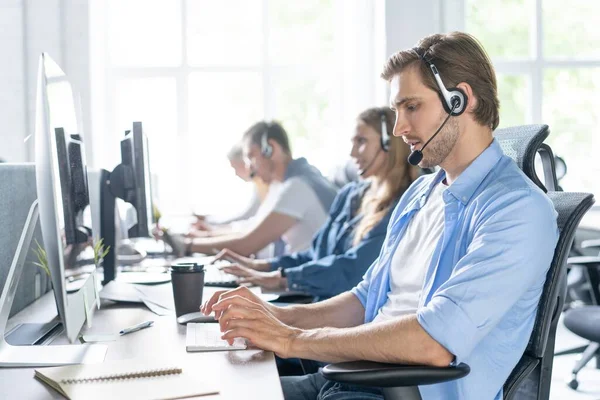 Jovem bonito masculino suporte ao cliente telefonista com fone de ouvido trabalhando no call center — Fotografia de Stock