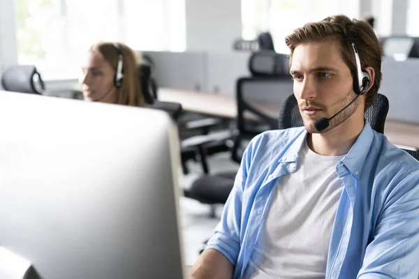 Joven guapo operador de atención al cliente masculino con auriculares trabajando en el centro de llamadas — Foto de Stock