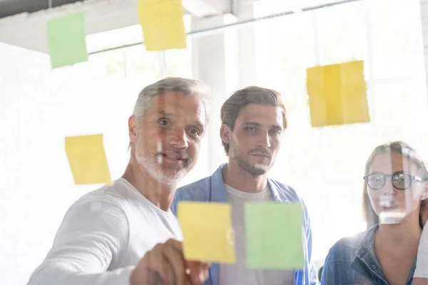 Las personas de negocios se reúnen en la oficina y usan notas postales para compartir ideas. Concepto de lluvia de ideas. Nota pegajosa en la pared de vidrio — Foto de Stock