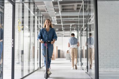 Modern açık uzay ofisinde scooter süren güzel genç bir kadın..