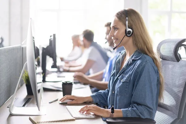 ¿Cómo puedo ayudarle Hermosos trabajadores del centro de llamadas en los auriculares están trabajando en la oficina moderna — Foto de Stock