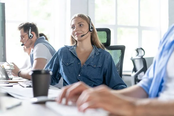 ¿Cómo puedo ayudarle Hermosos trabajadores del centro de llamadas en los auriculares están trabajando en la oficina moderna —  Fotos de Stock