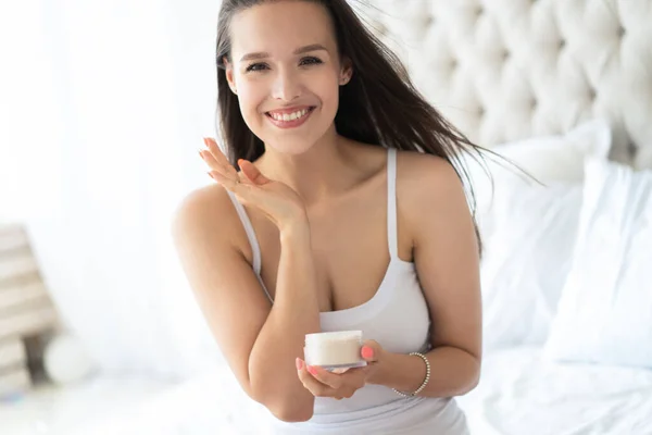 Morena bonita usando creme corporal na cama em casa . — Fotografia de Stock