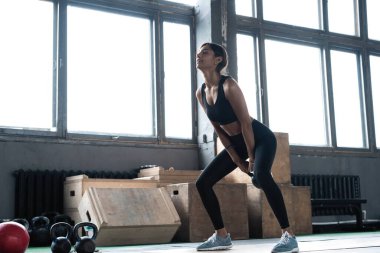 Spor giyim kuşağında harika vücudu olan genç ve güzel bir kadın spor salonunda çaydanlık çanlarıyla çalışıyor..