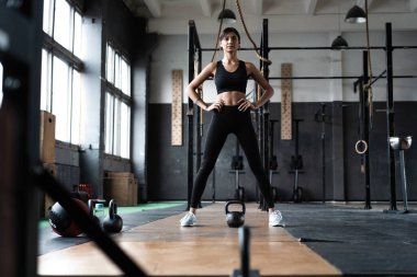 Formda bir spor salonunda dikilip bakışlarını kaçıran güçlü bir kadın. Spor giyim sektöründe kendine güvenen bir kadın model..