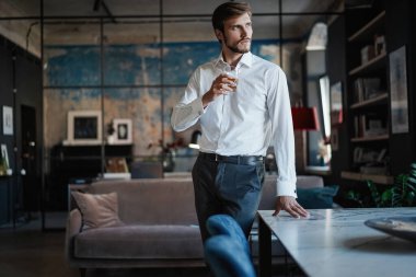 Genç yakışıklı işadamı dikilip kendi ofisinde bir bardak viski tutuyor..