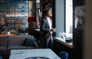 Genç yakışıklı işadamı dikilip kendi ofisinde bir bardak viski tutuyor..